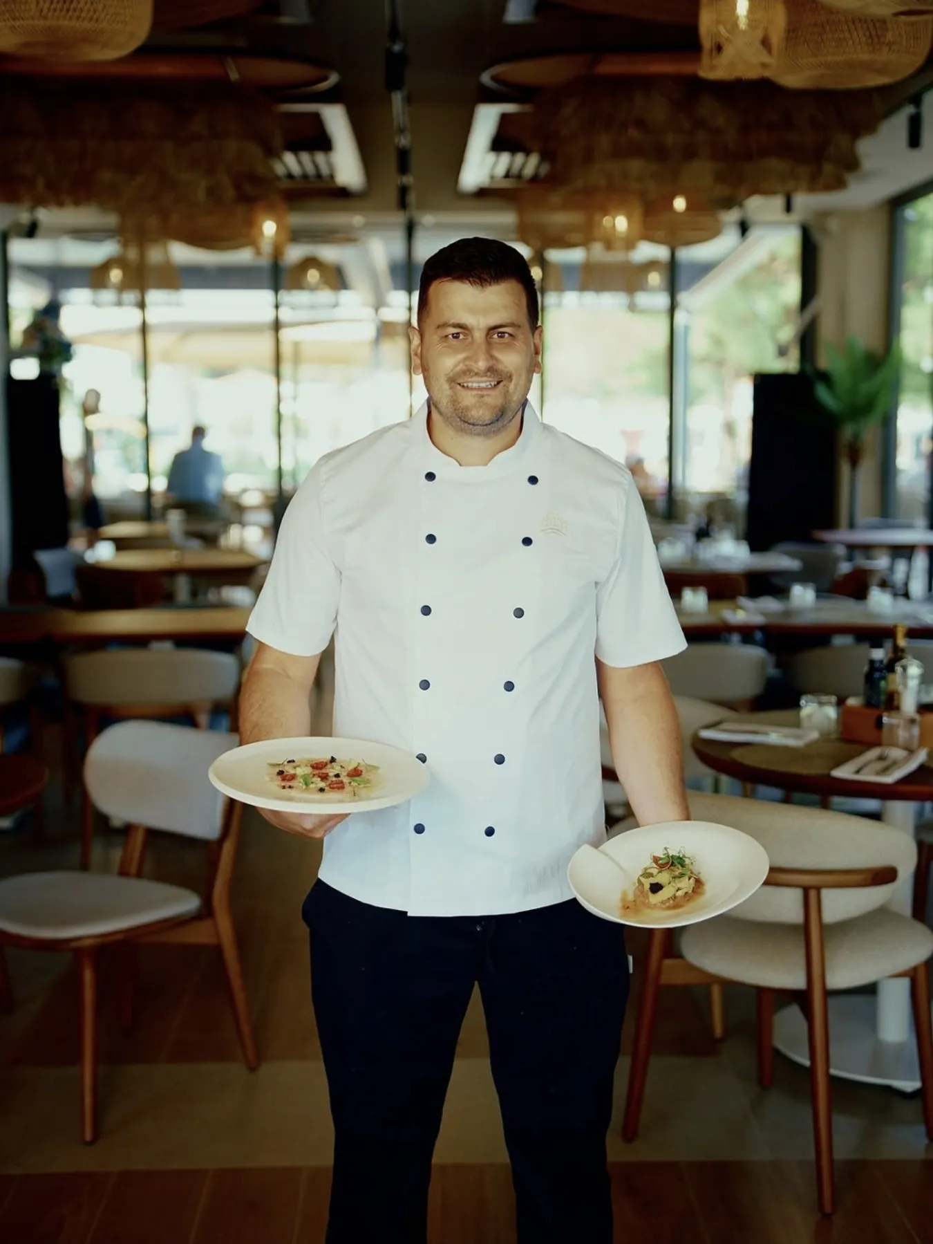 Miloš Ristić u kuvarskoj bluzi u restoranu, sa serviranim tanjirima.